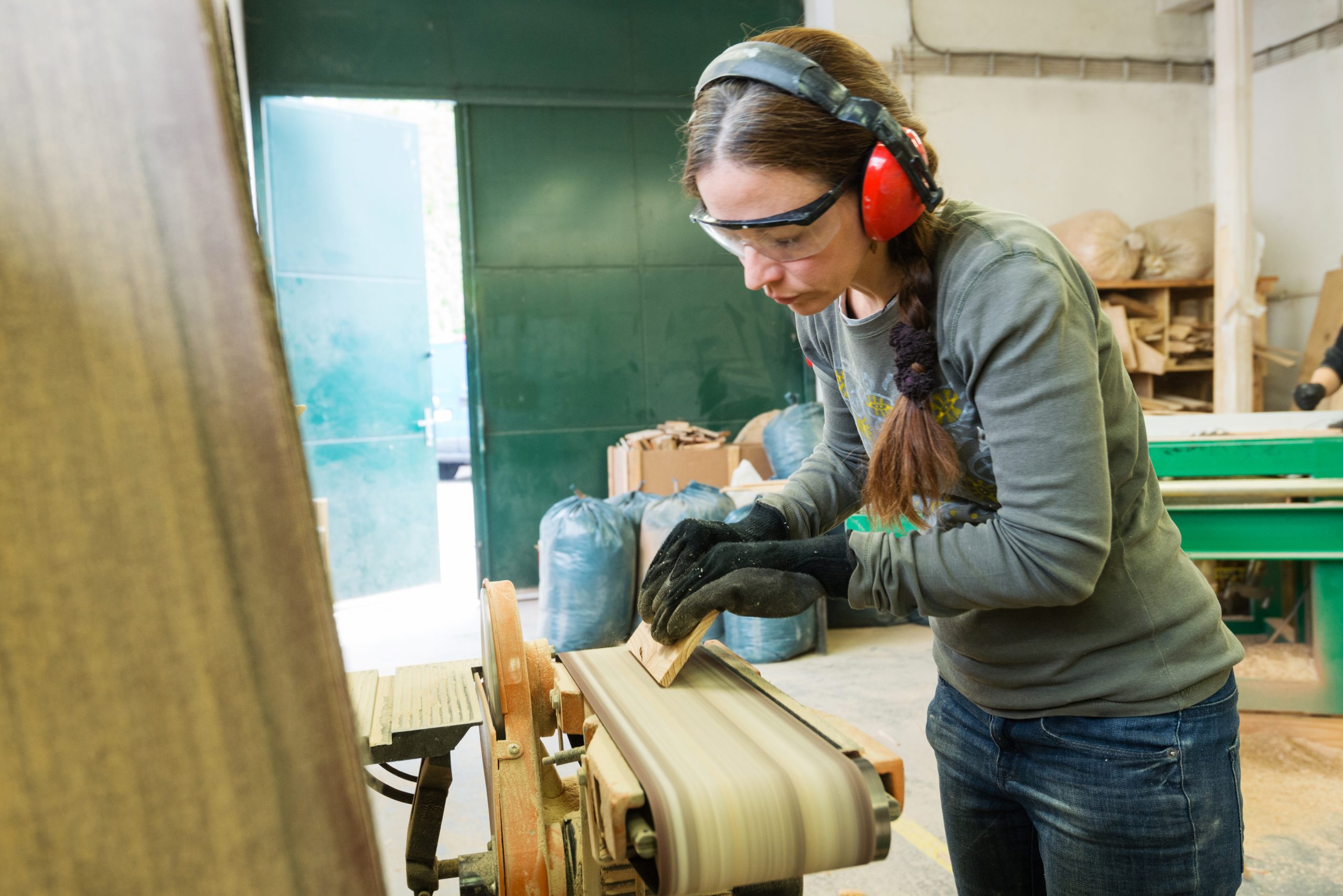 Young woman using a belt sander to sand wooden plank at workshop